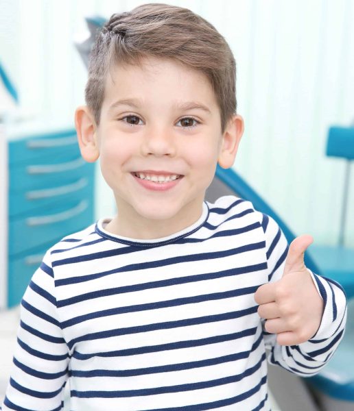 Cute little boy showing thumb up sign at dentist's office